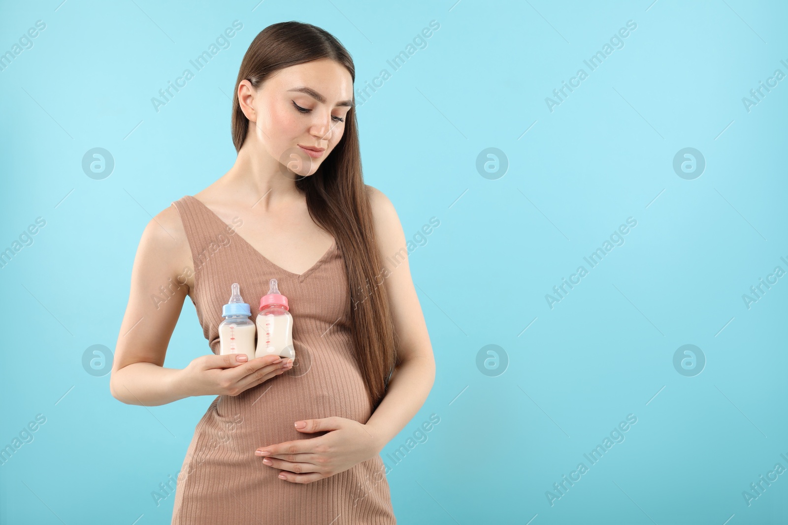 Photo of Expecting twins. Pregnant woman holding two bottles with milk on light blue background, space for text