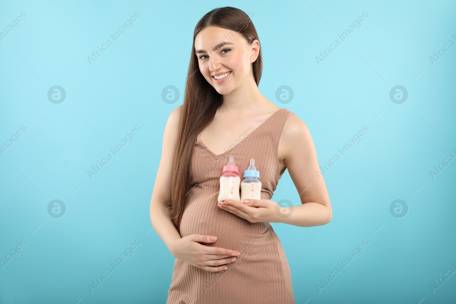 Photo of Expecting twins. Pregnant woman holding two bottles with milk on light blue background