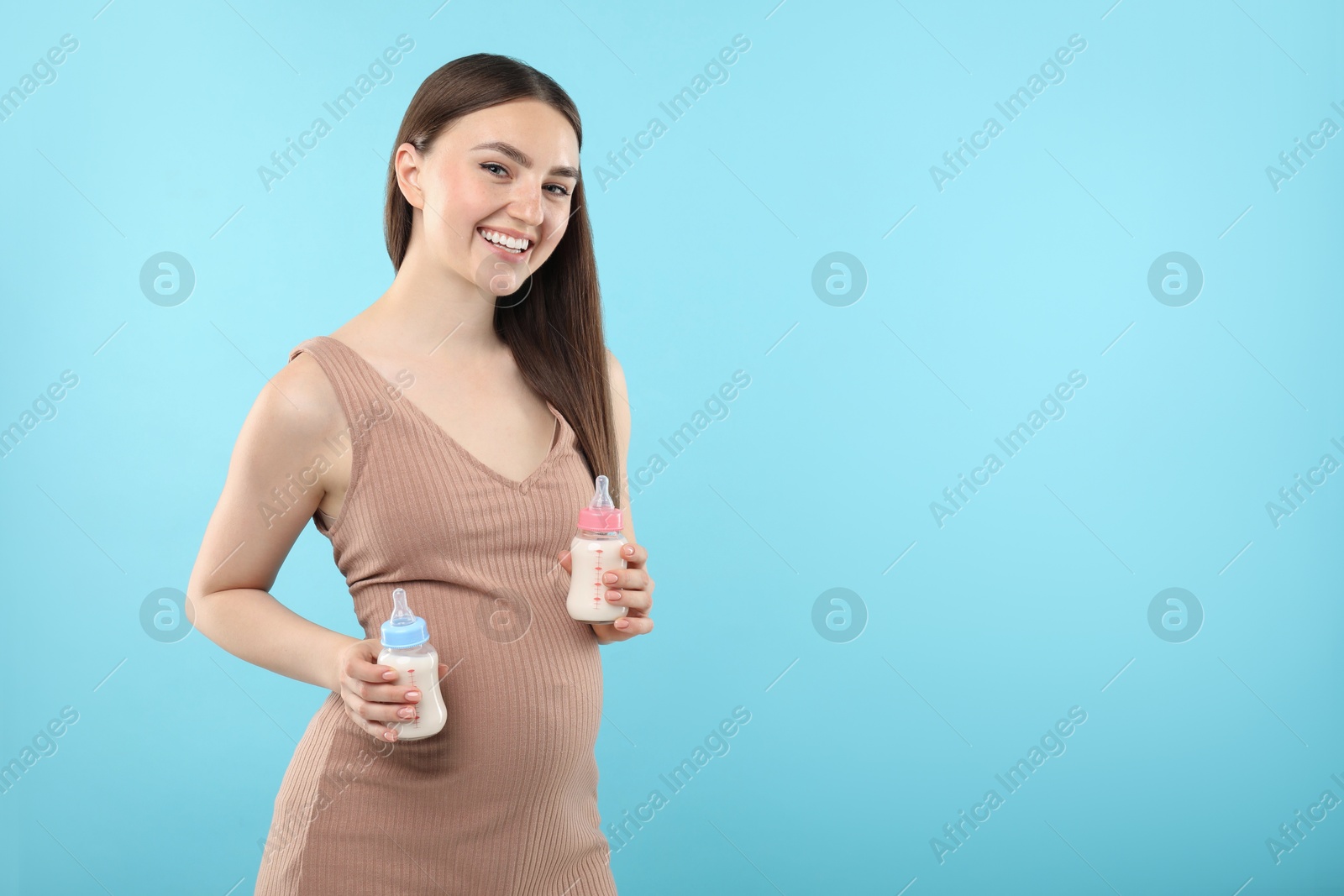 Photo of Expecting twins. Pregnant woman holding two bottles with milk on light blue background, space for text