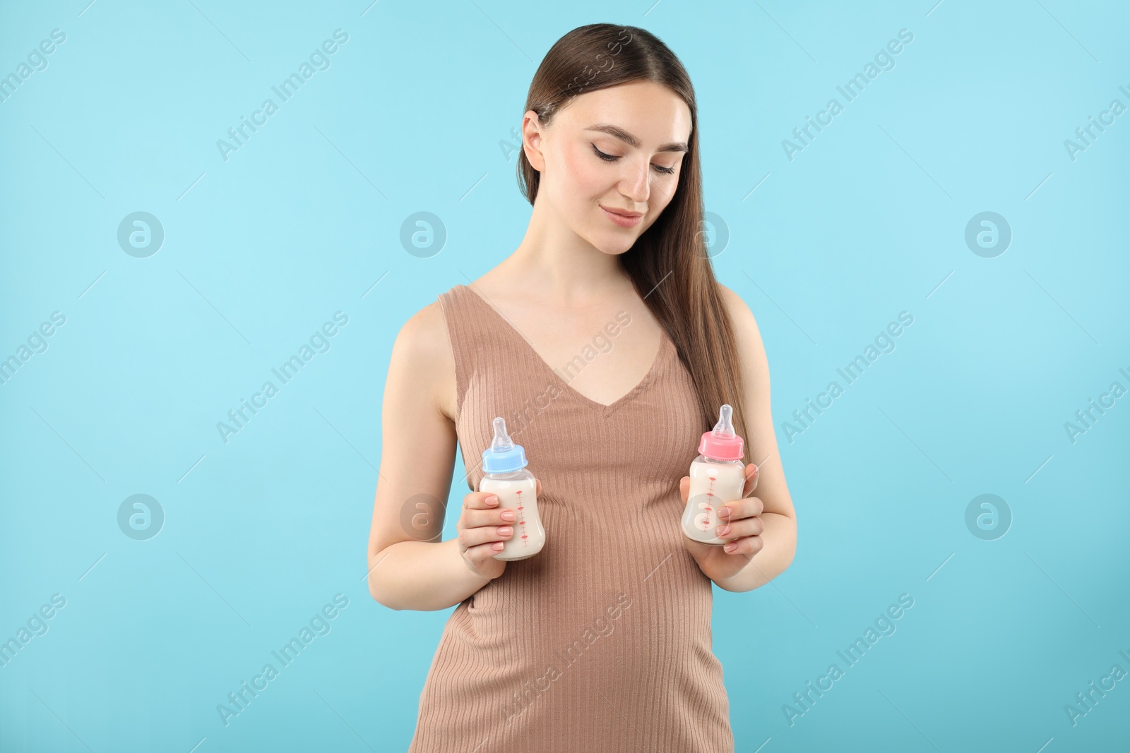 Photo of Expecting twins. Pregnant woman holding two bottles with milk on light blue background