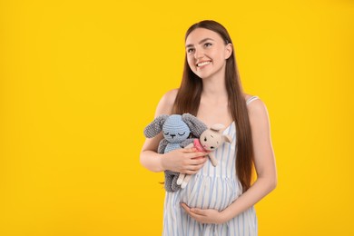 Photo of Expecting twins. Pregnant woman holding two toys on yellow background, space for text