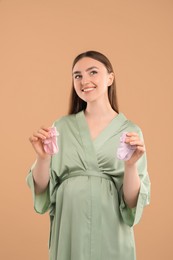 Photo of Expecting twins. Pregnant woman holding two pairs of socks on light brown background