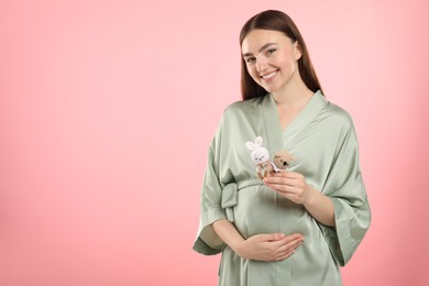 Photo of Expecting twins. Pregnant woman holding two toys on pink background, space for text