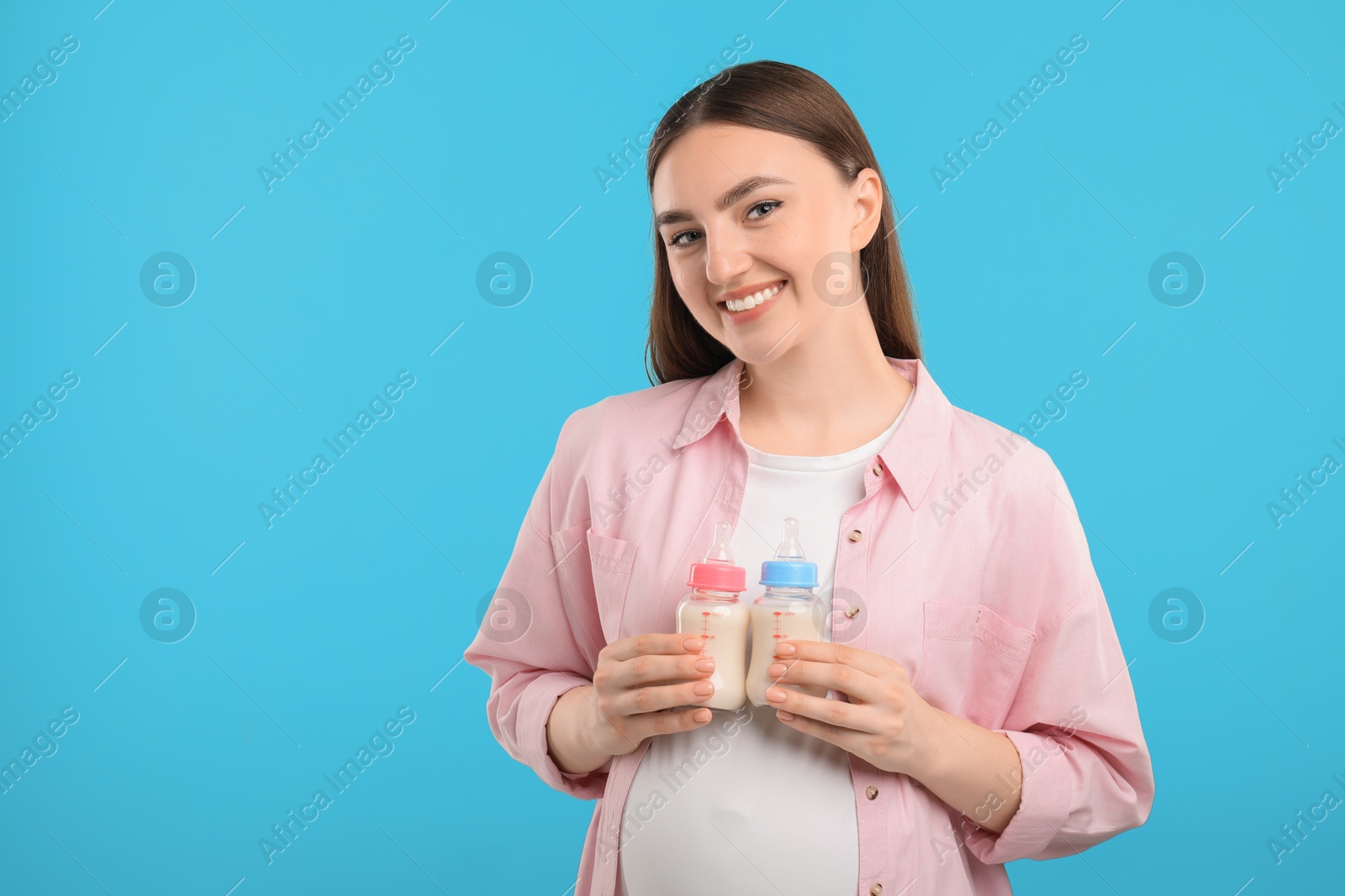 Photo of Expecting twins. Pregnant woman holding two bottles with milk on light blue background, space for text