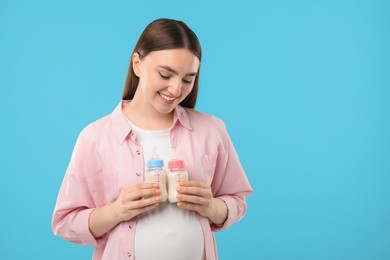 Photo of Expecting twins. Pregnant woman holding two bottles with milk on light blue background, space for text