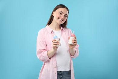 Photo of Expecting twins. Pregnant woman holding two bottles with milk on light blue background