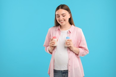Photo of Expecting twins. Pregnant woman holding two bottles with milk on light blue background