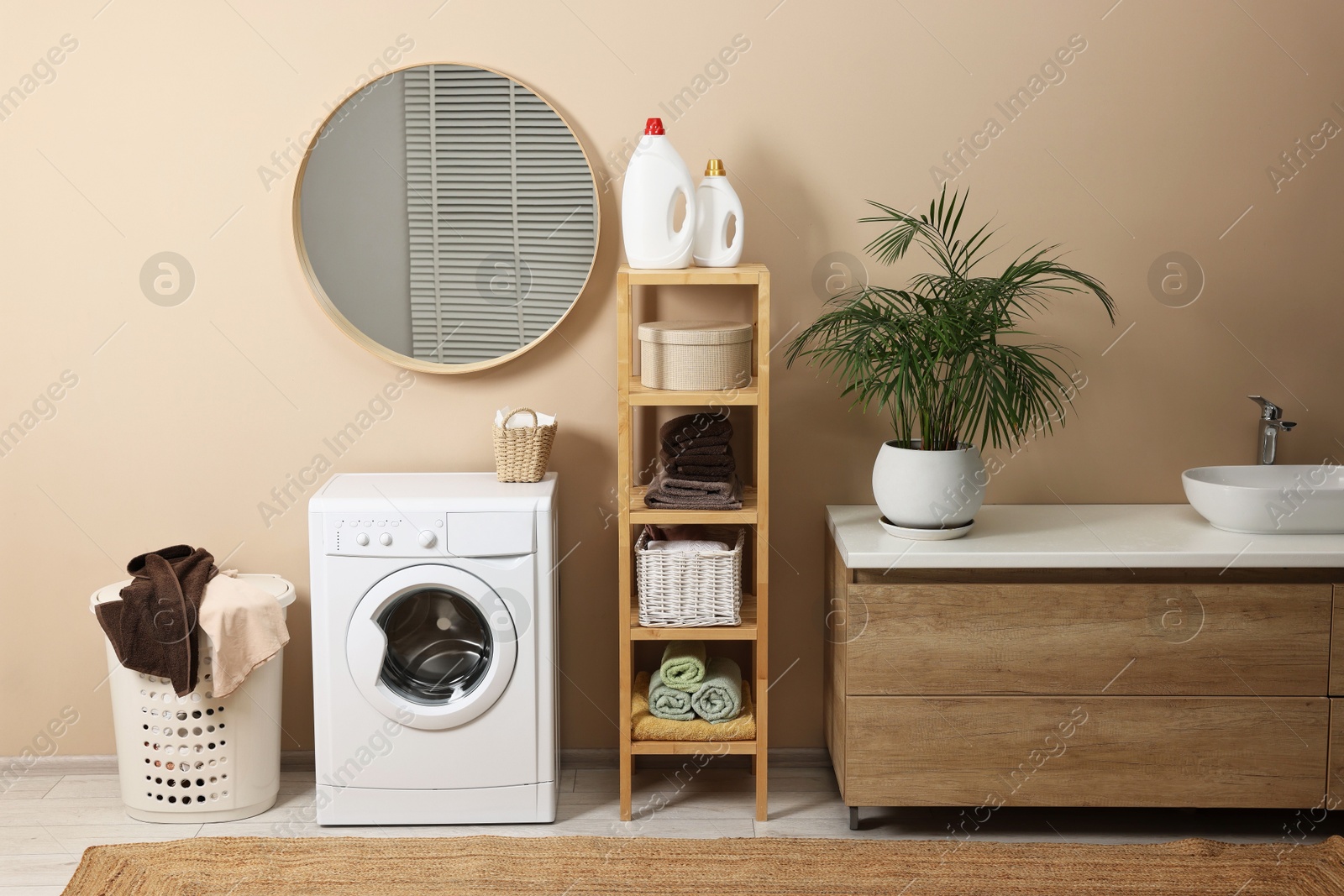 Photo of Stylish laundry room interior with washing machine, vessel sink, houseplant and basket