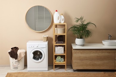 Photo of Stylish laundry room interior with washing machine, vessel sink, houseplant and basket