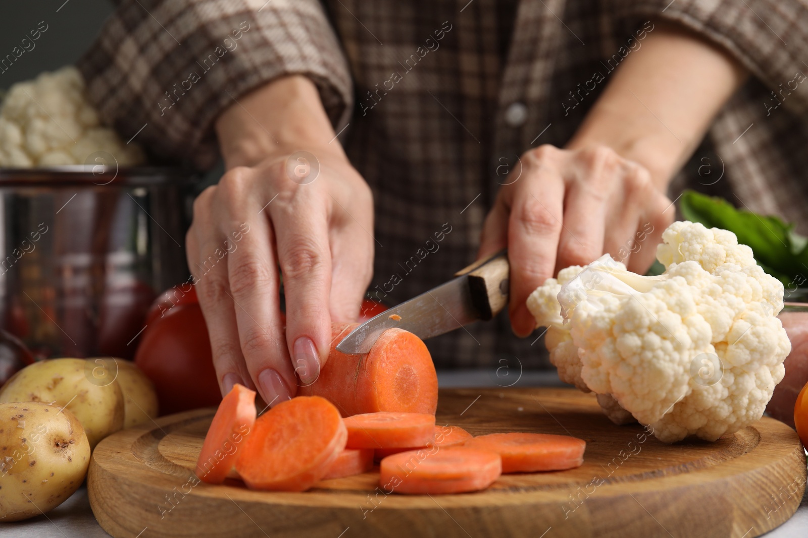 Photo of Cooking vegetable stew. Woman cutting carrot at table, closeup