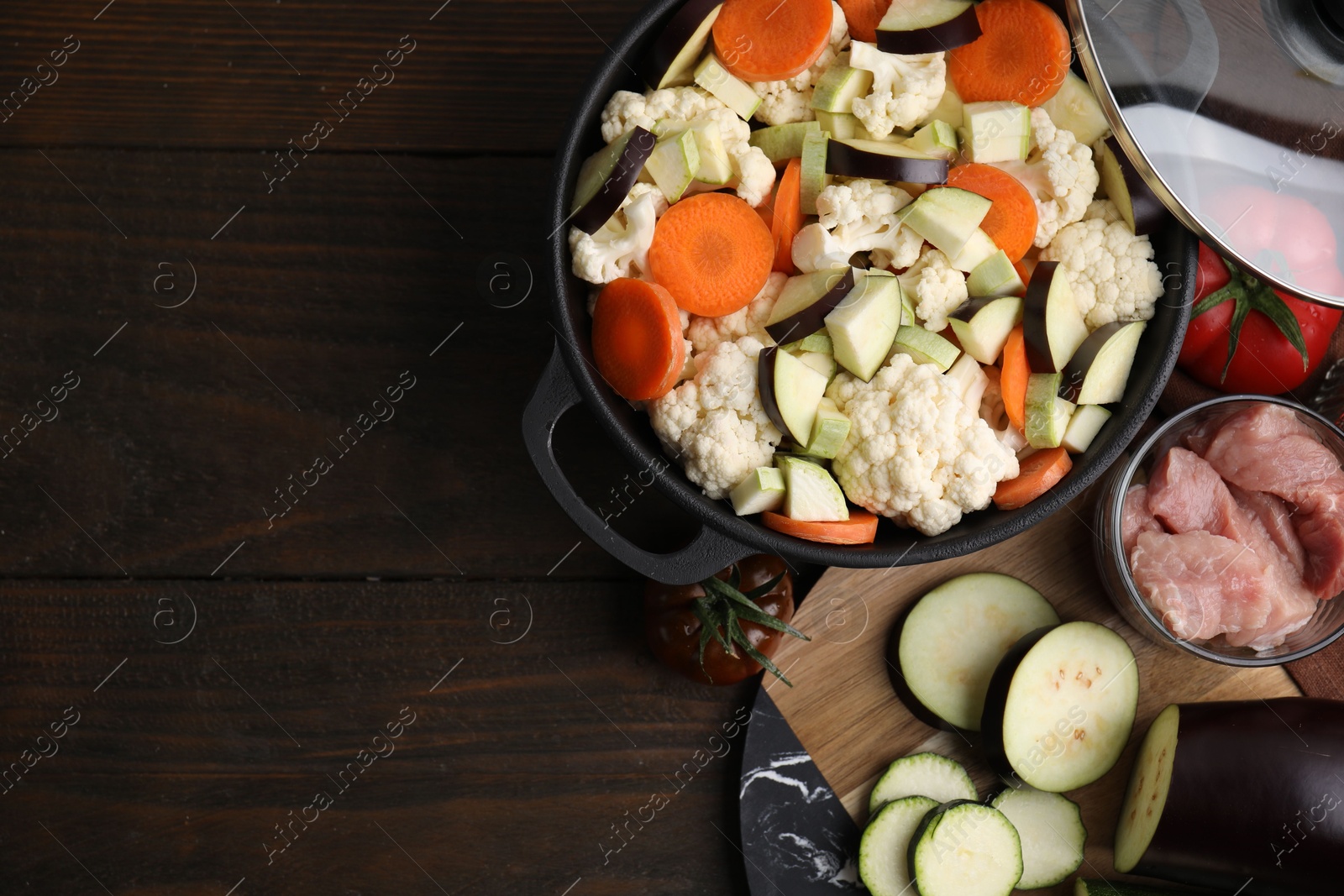 Photo of Cooking stew. Cut raw vegetables in pot and meat on wooden table, flat lay