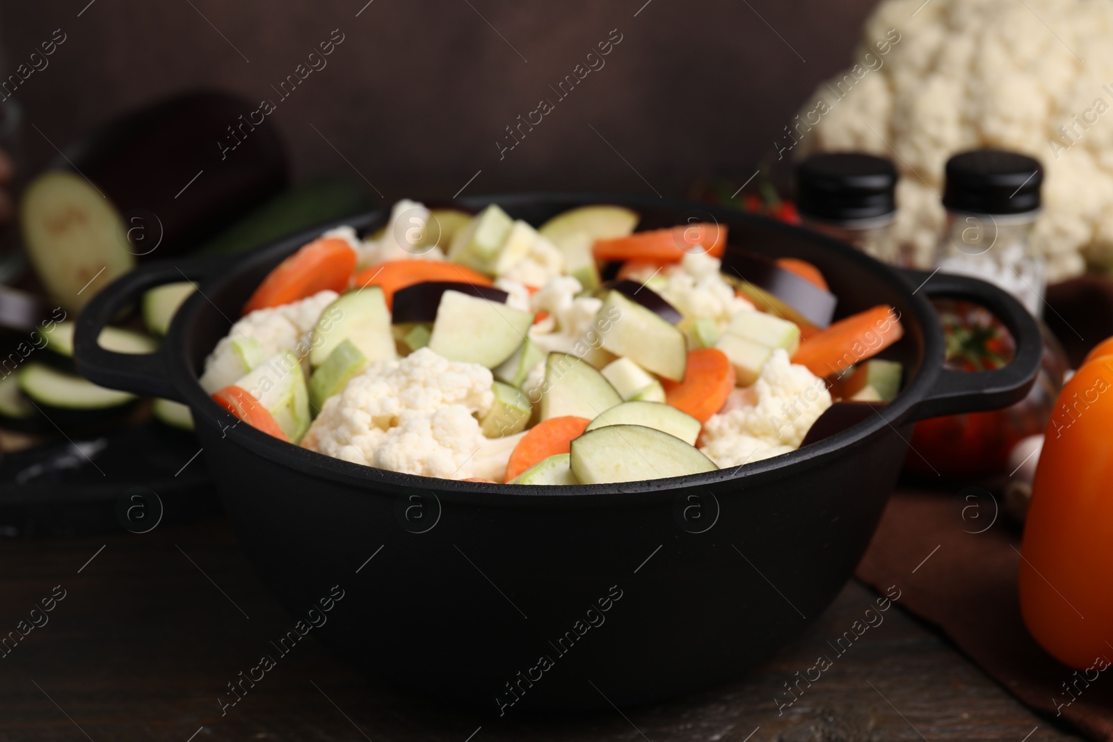 Photo of Cooking stew. Cut raw vegetables in pot on wooden table, closeup