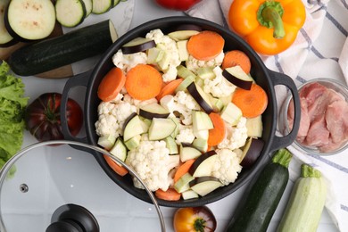 Cooking stew. Cut raw vegetables in pot and other ingredients on white tiled table, flat lay