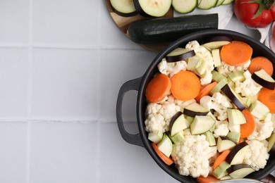 Photo of Cooking stew. Cut raw vegetables in pot on white tiled table, flat lay