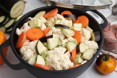 Photo of Cooking stew. Cut raw vegetables in pot and other ingredients on white table, closeup