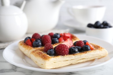 Photo of Tasty puff pastries with berries and tea on white marble table, closeup