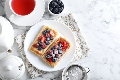 Photo of Tasty puff pastries with berries and tea on white marble table, flat lay. Space for text