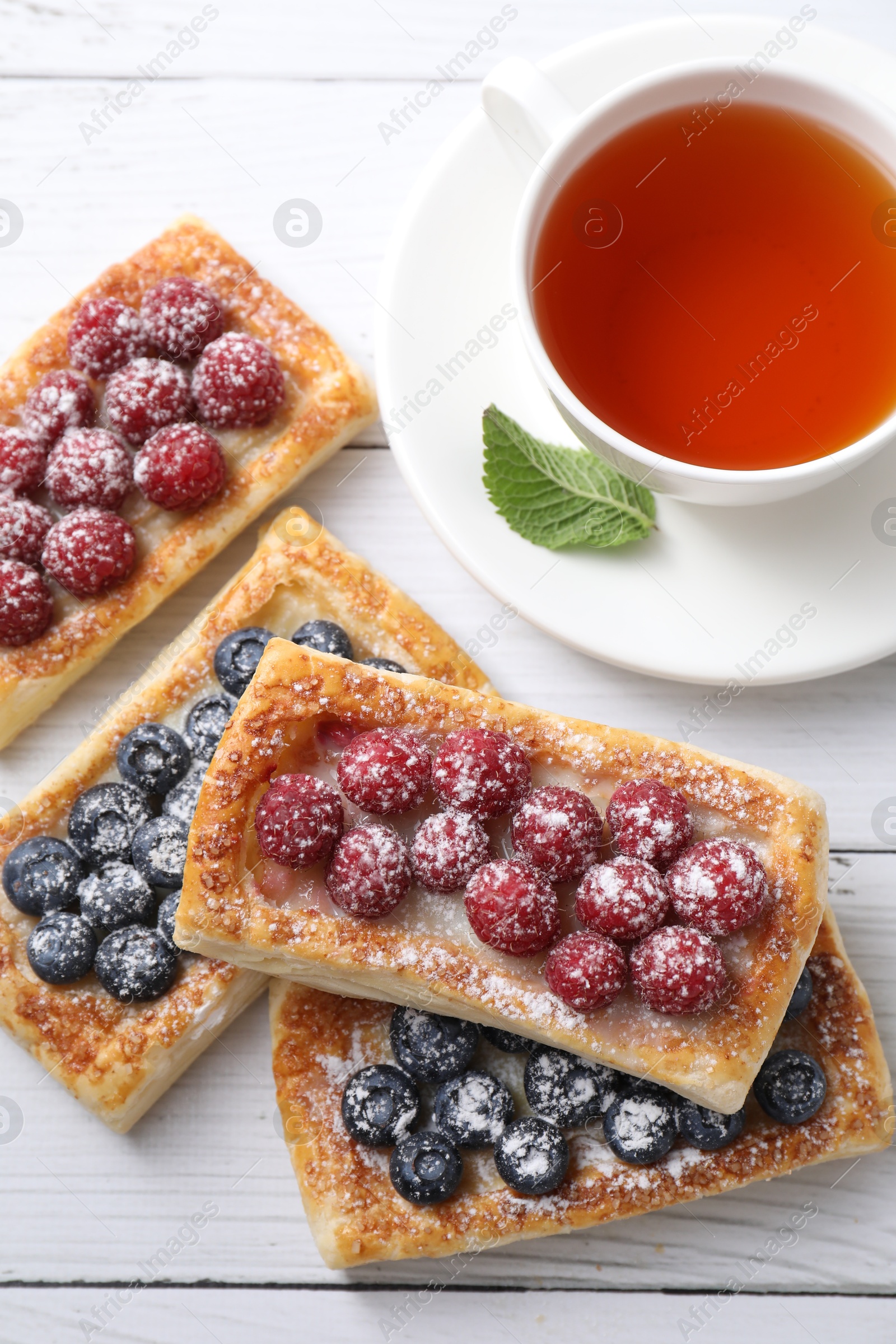 Photo of Tasty puff pastries with berries and tea on white wooden table, flat lay