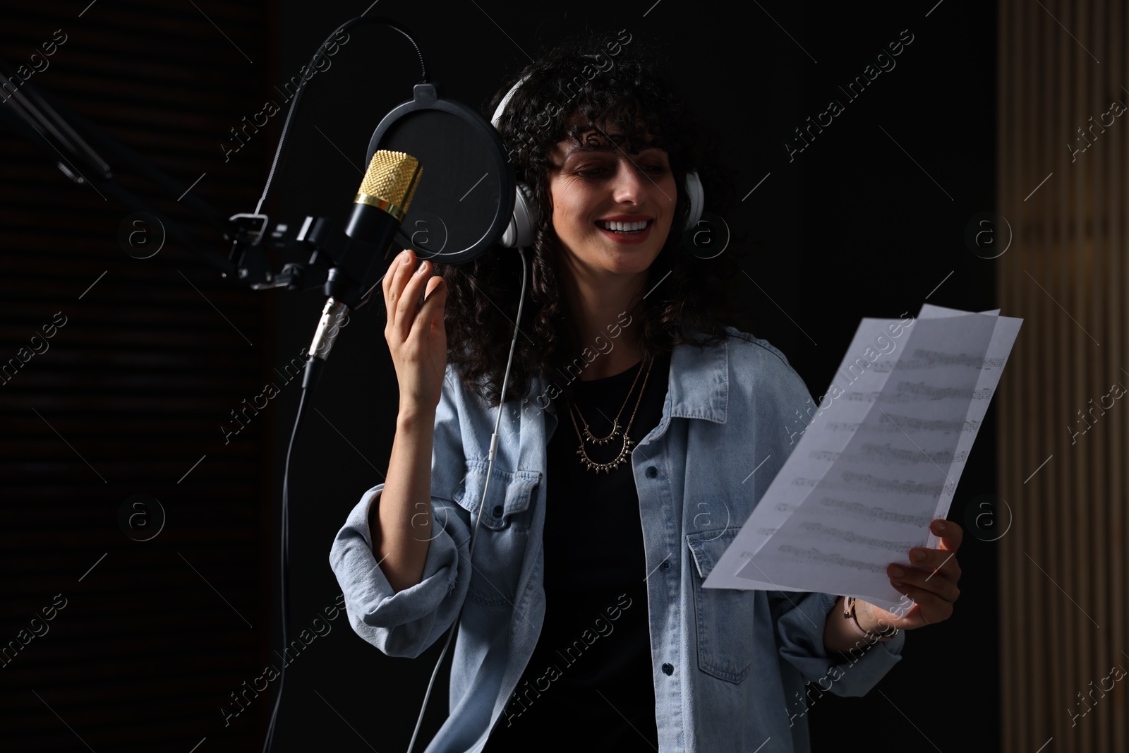 Photo of Singer wearing headphones recording song in professional studio