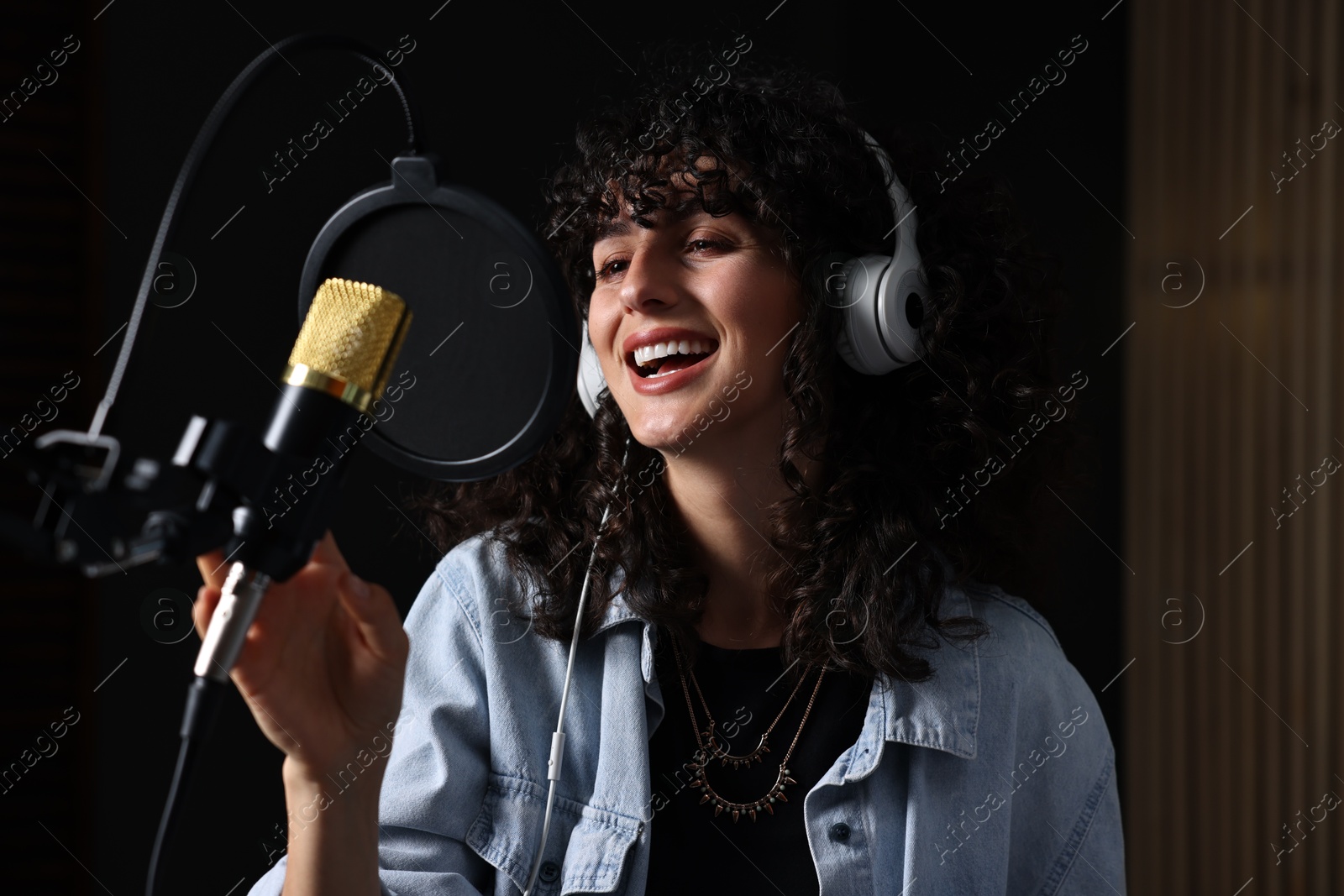 Photo of Vocalist with headphones singing into microphone in professional record studio