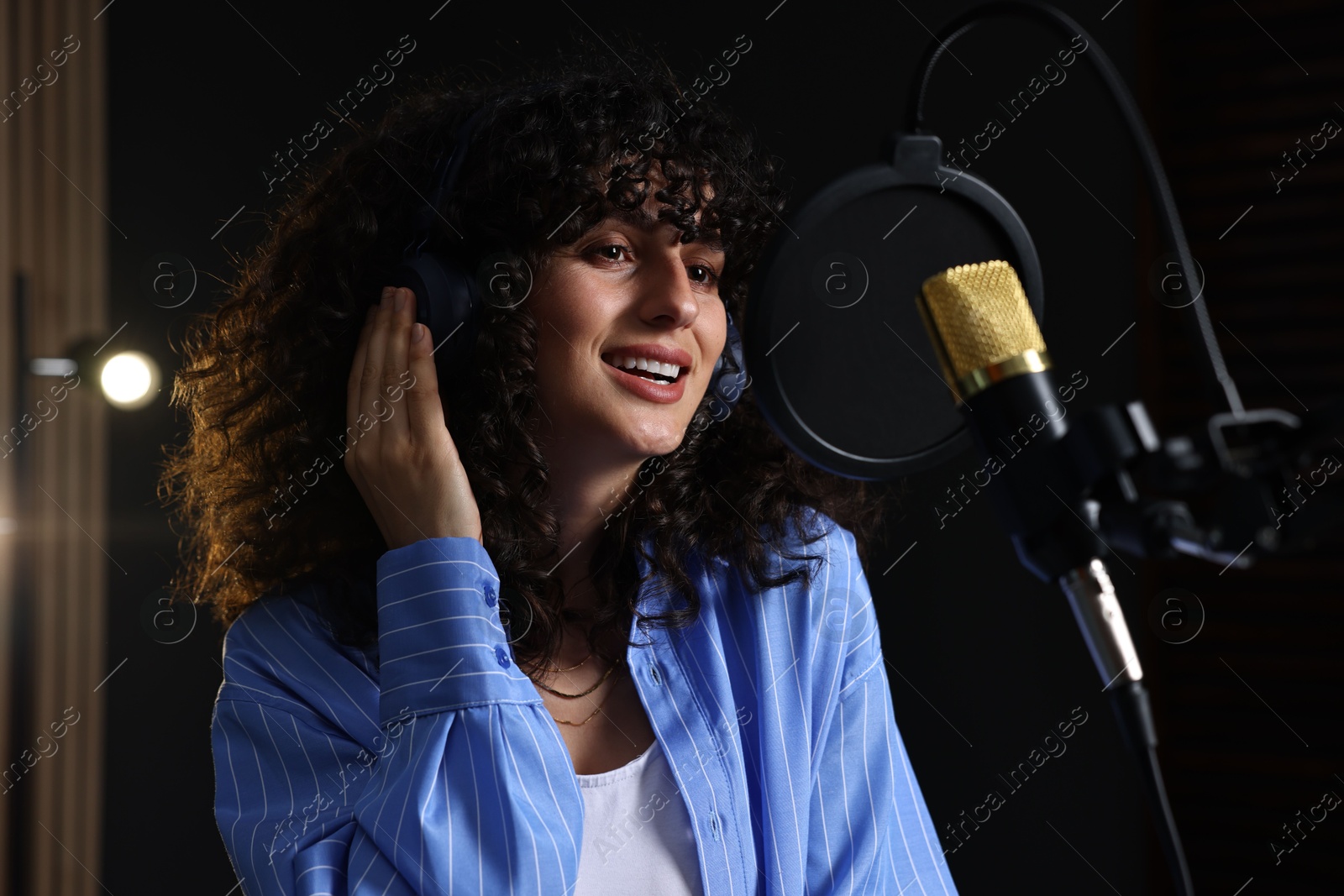 Photo of Vocalist with headphones singing into microphone in professional record studio