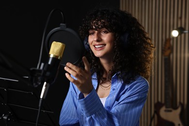 Photo of Singer with headphones recording song in professional studio