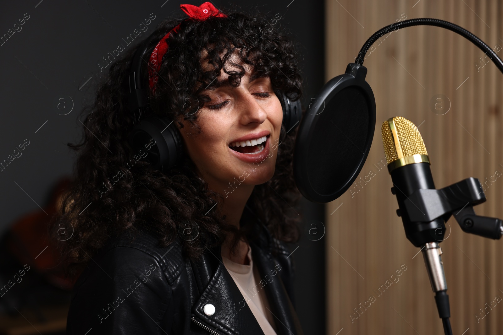 Photo of Vocalist with headphones singing into microphone in professional record studio