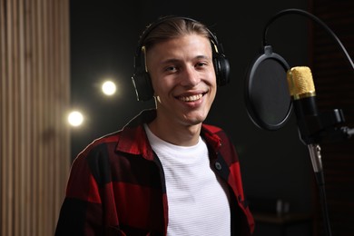 Photo of Singer with headphones recording song in professional studio