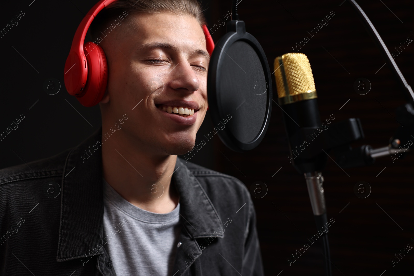 Photo of Vocalist with headphones singing into microphone in professional record studio