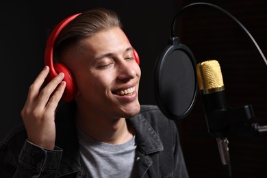 Photo of Man wearing headphones singing into microphone in professional record studio