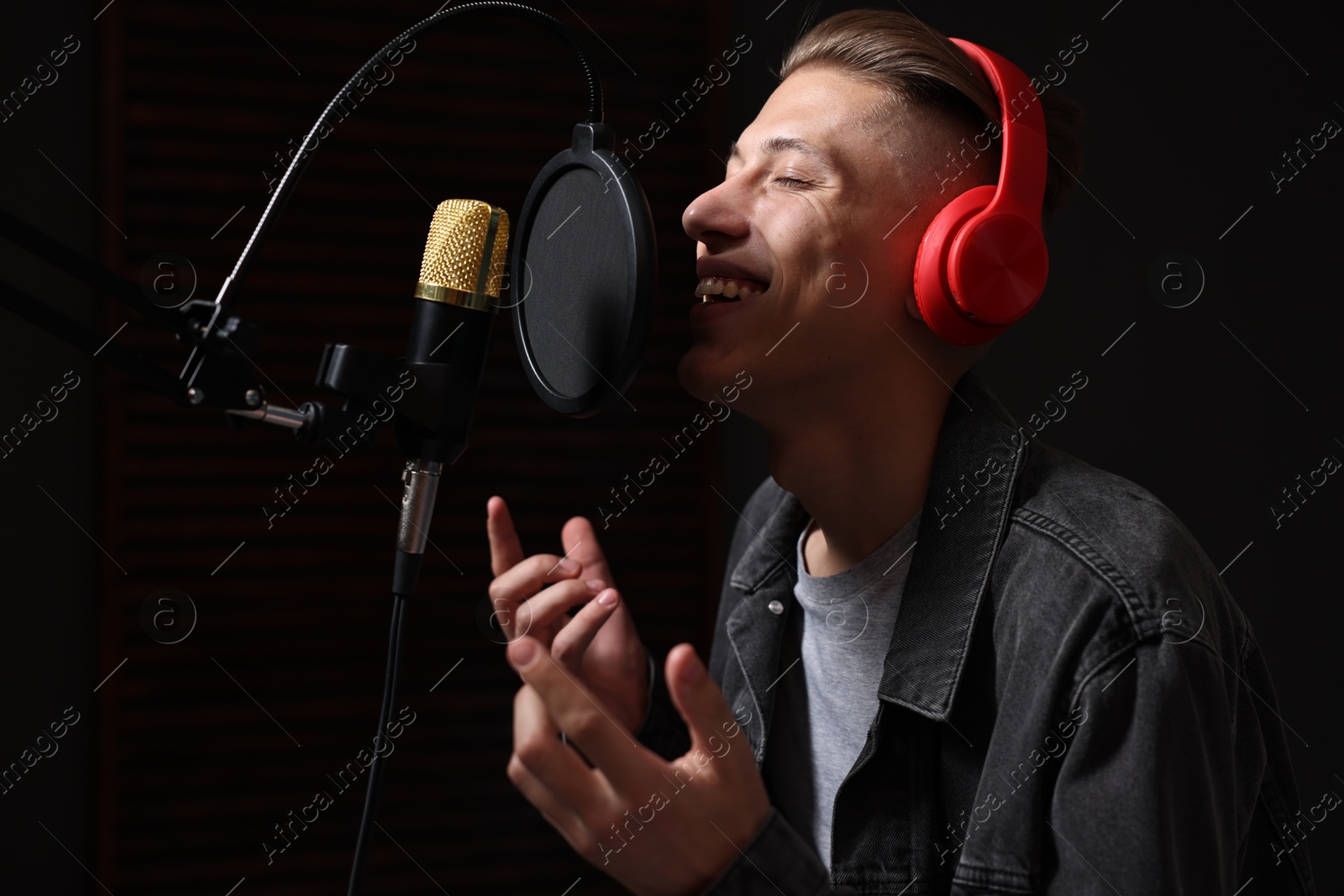 Photo of Vocalist with headphones singing into microphone in professional record studio