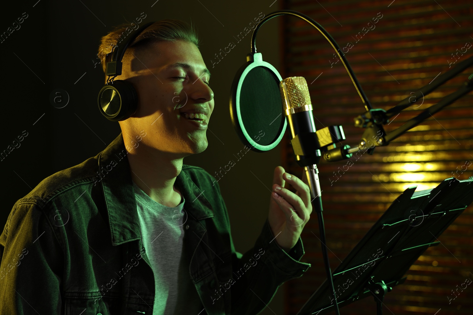 Photo of Vocalist with headphones singing into microphone in professional record studio