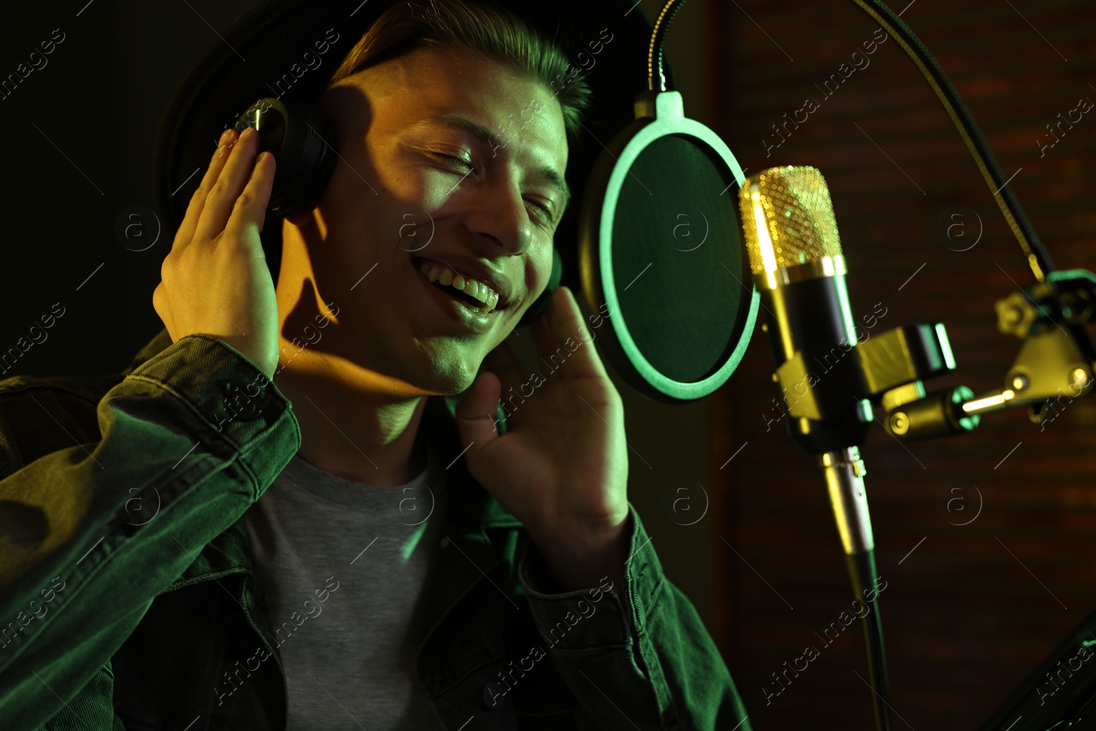 Photo of Vocalist with headphones singing into microphone in professional record studio