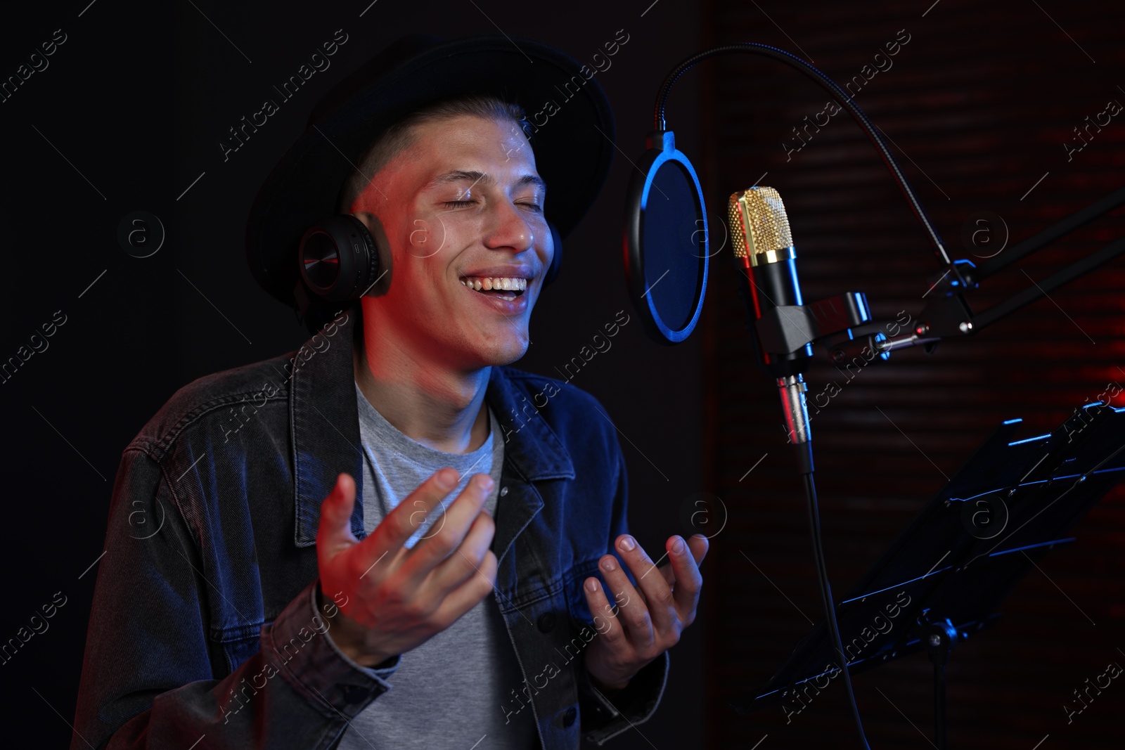 Photo of Vocalist with headphones singing into microphone in professional record studio