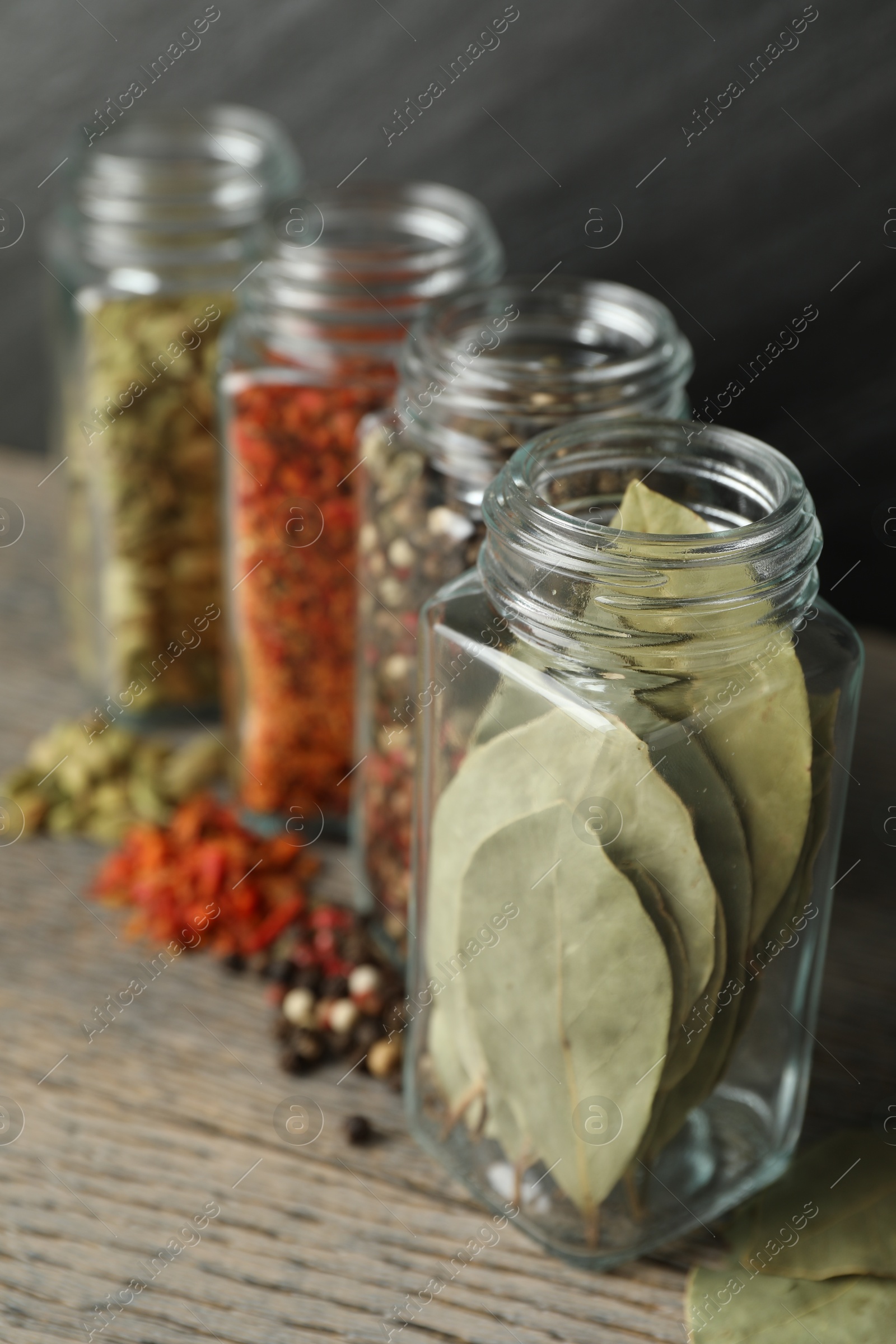 Photo of Different spices in glass jars on grey wooden table, closeup