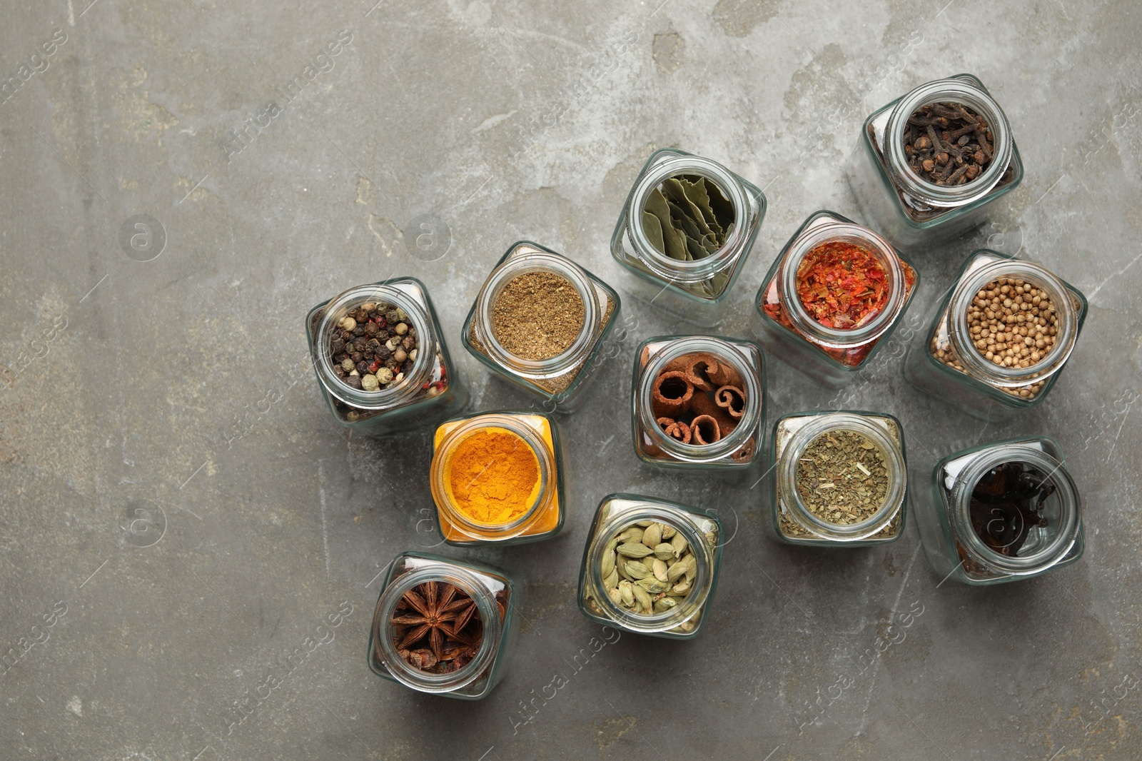 Photo of Different spices in glass jars on grey table, flat lay