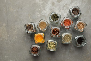 Different spices in glass jars on grey table, flat lay