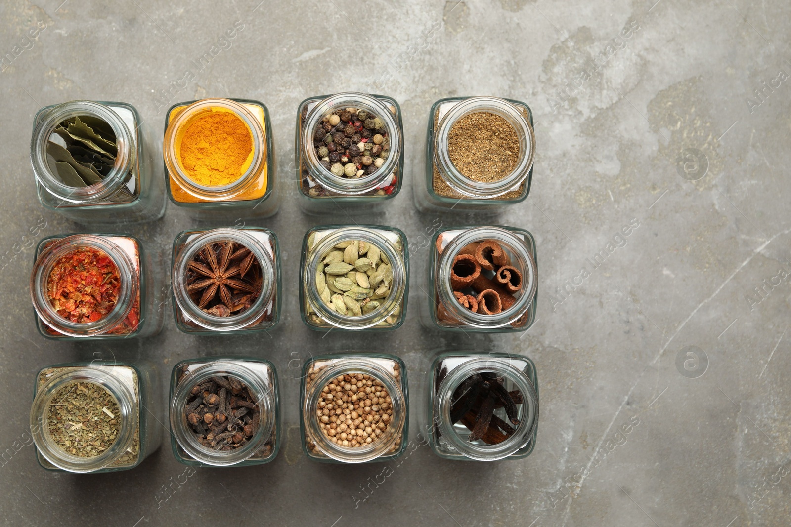 Photo of Different spices in glass jars on grey table, flat lay. Space for text