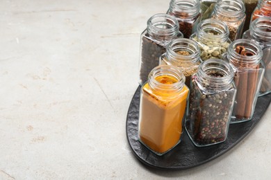 Different spices in glass jars on light grey table, space for text