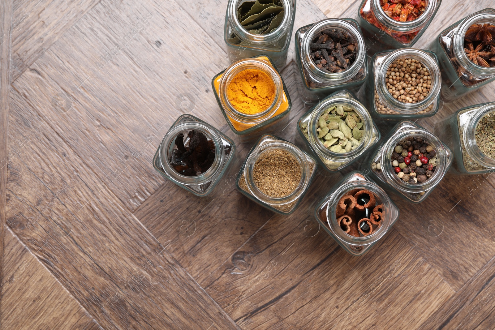 Photo of Different spices in glass jars on wooden table, flat lay. Space for text