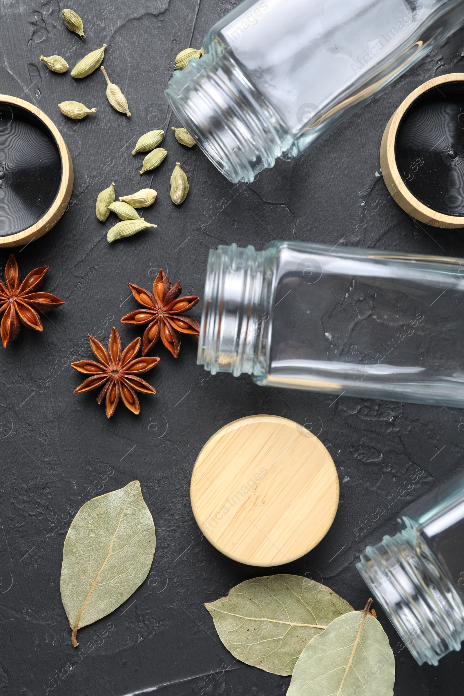 Photo of Different spices and glass jars on black table, flat lay