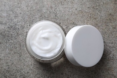 Face cream in jar on grey textured table, top view