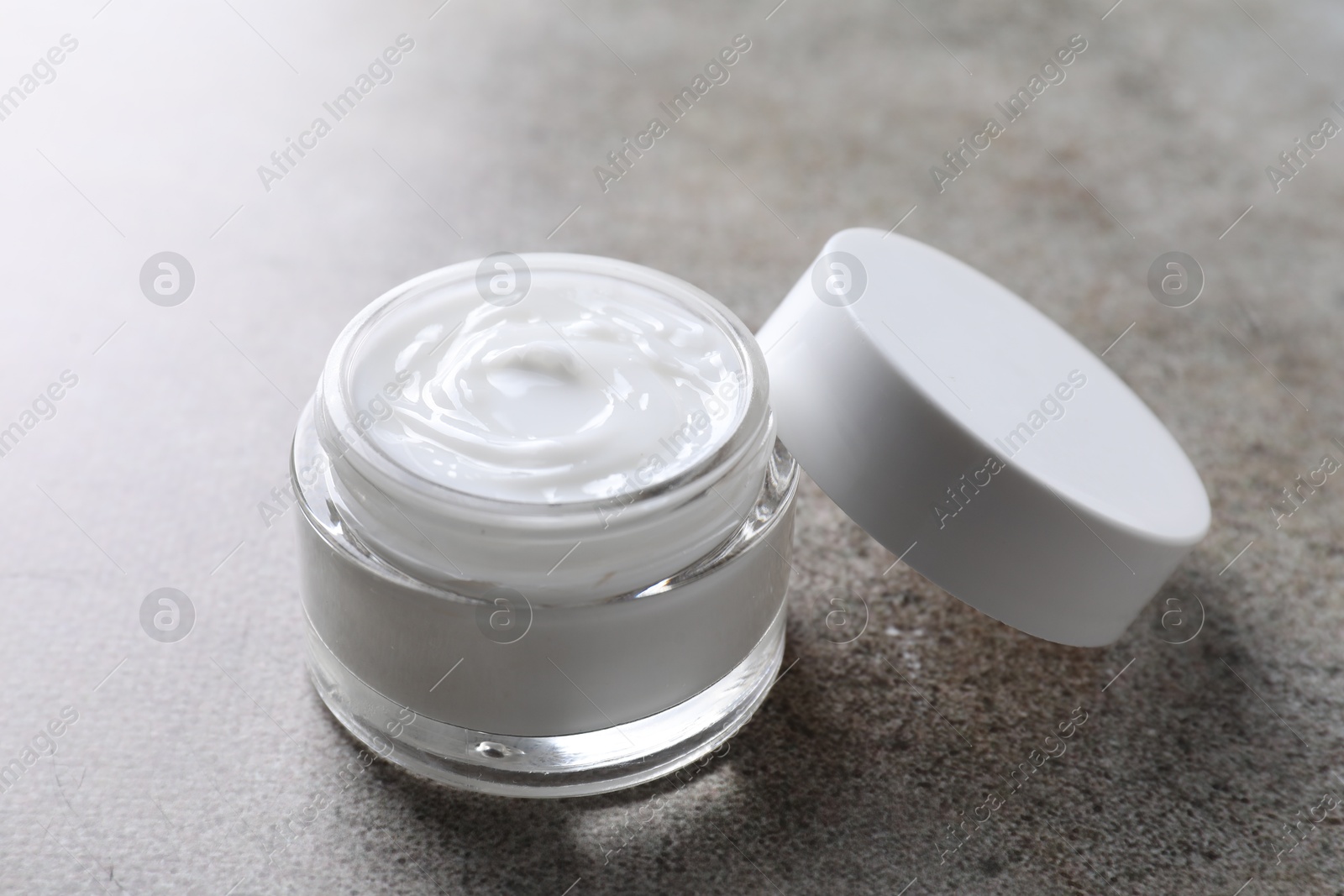 Photo of Face cream in jar on grey textured table, closeup