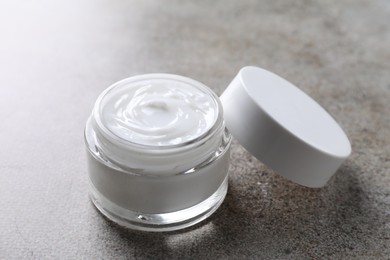 Face cream in jar on grey textured table, closeup