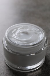 Face cream in jar on grey textured table, closeup