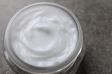 Photo of Face cream in jar on grey textured table, closeup