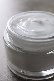 Face cream in jar on grey table, closeup