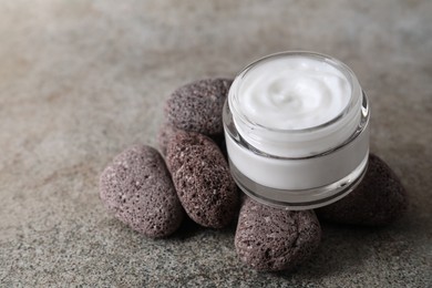 Photo of Face cream in jar and stones on grey textured table, closeup. Space for text