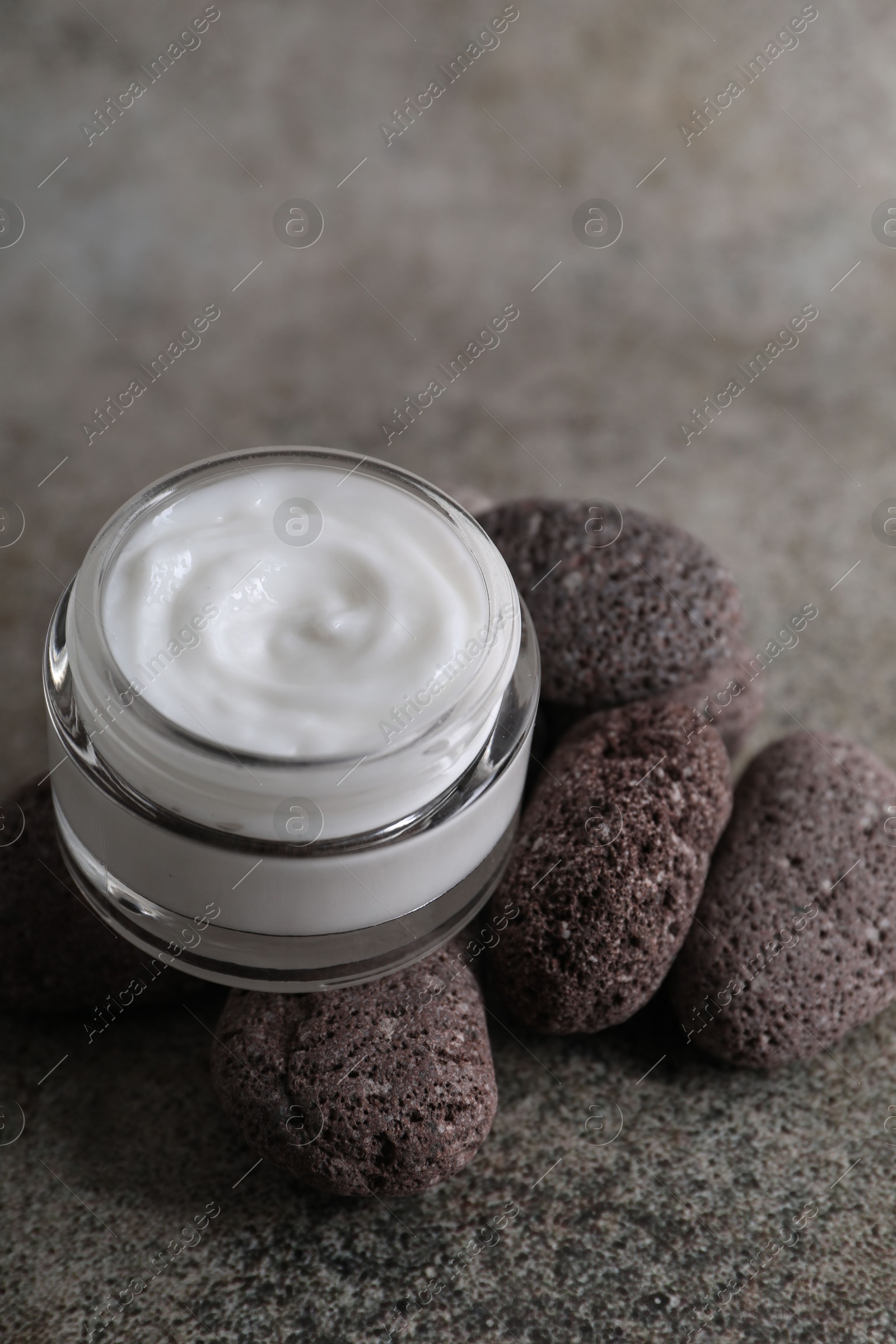 Photo of Face cream in jar and stones on grey textured table, closeup