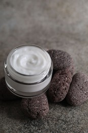 Face cream in jar and stones on grey textured table, closeup